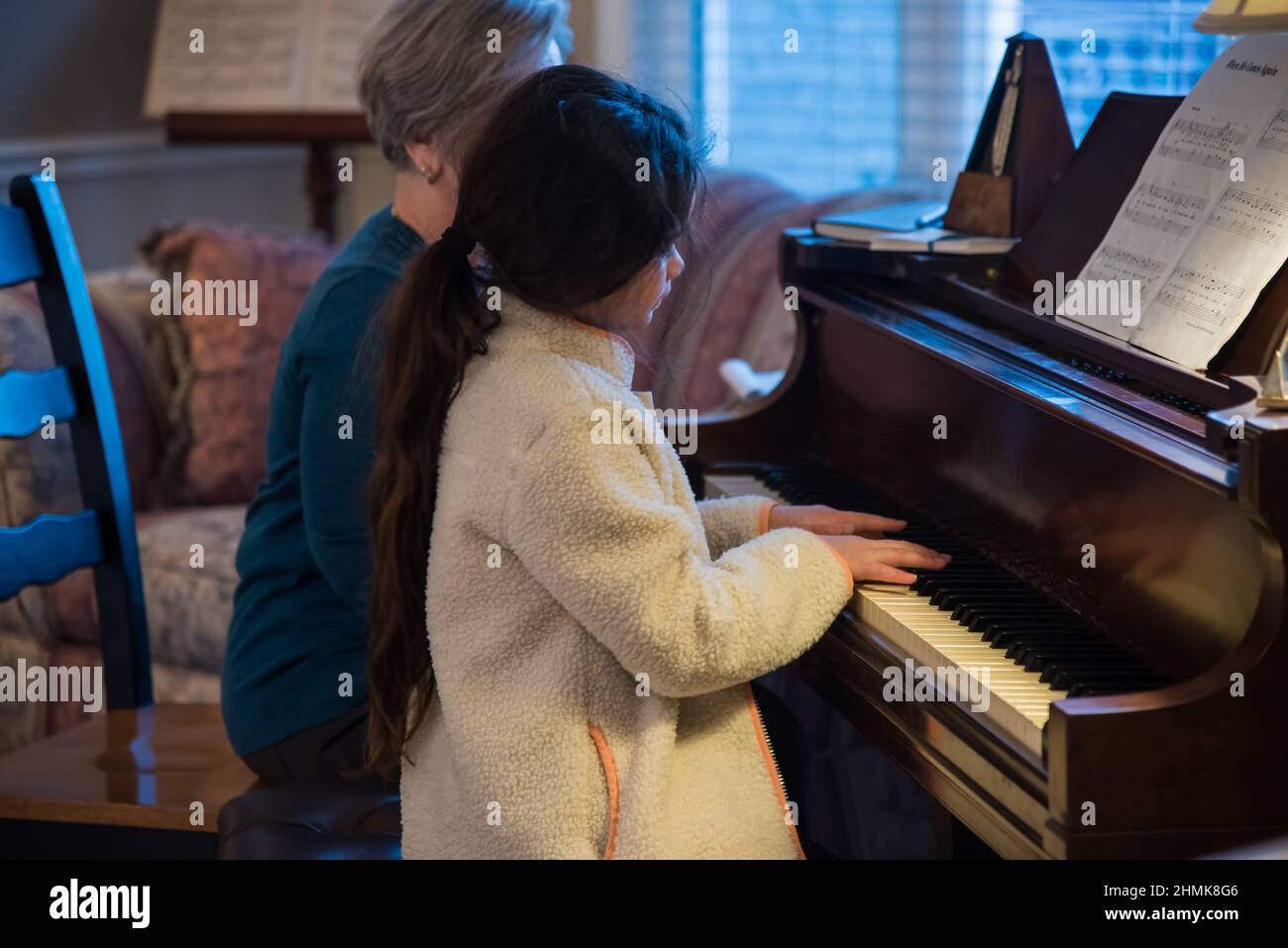 South Jordan, Utah, USA, Feb. 10, 2022.  A beautiful young piano student concentrates on her lesson.  Her teacher watches her every move. Stock Photo