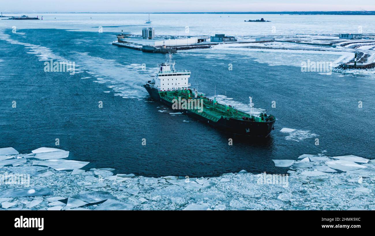 Enormous cargo ship sailing through ocean water with thick layer of broken ice pieces covering surface on polar day aerial view Stock Photo