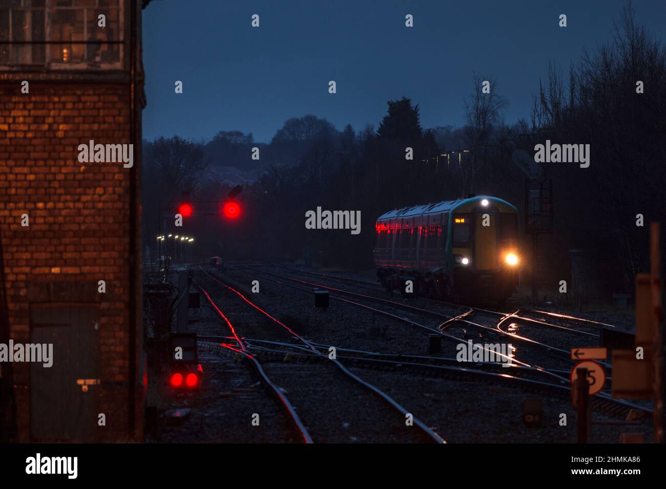 London midland Bombardier class 172 train with its headlights glinting on the track and red signals at Stourbridge junction on a dark wet night Stock Photo
