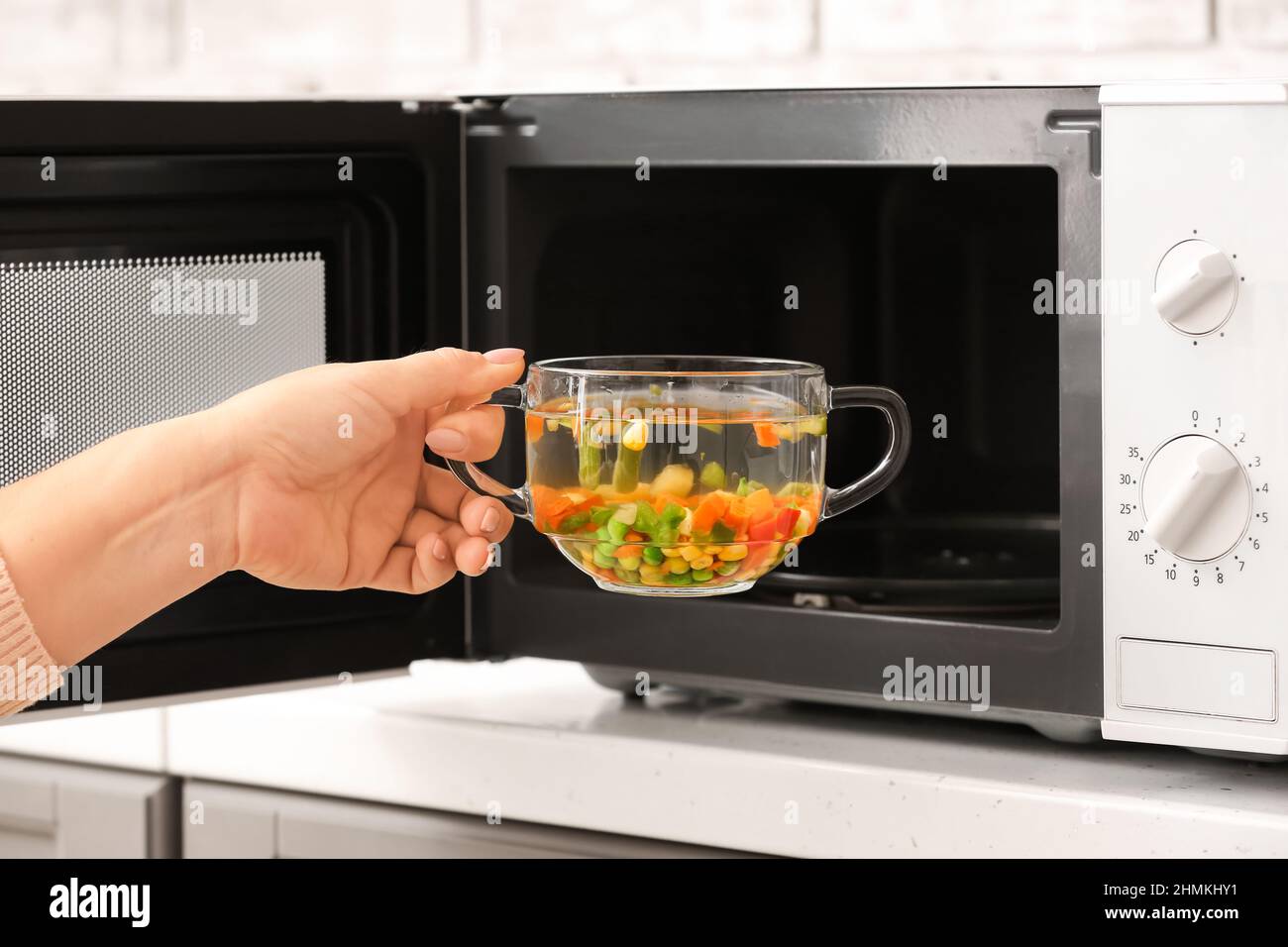 Woman putting glass bowl with broth into microwave oven, closeup Stock