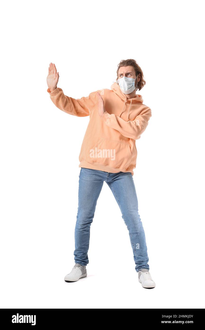 Young man in medical mask avoiding something on white background Stock Photo