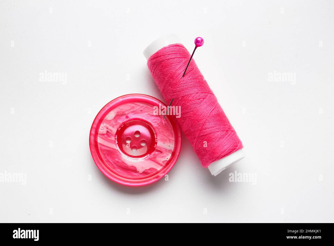 Thread spool with button and needle on white background Stock