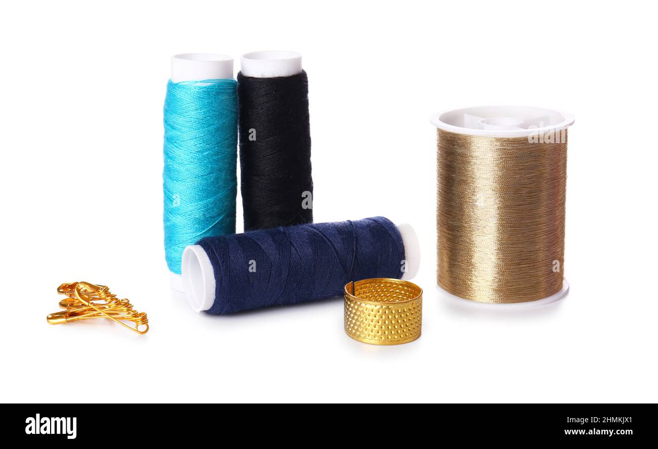 Different thread spools, thimble and safety pins on white background Stock Photo
