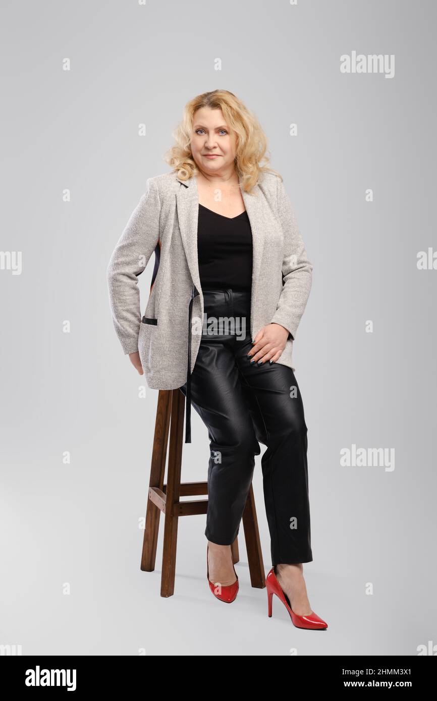Portrait of senior woman in leather trousers and blazer sitting on tall ...