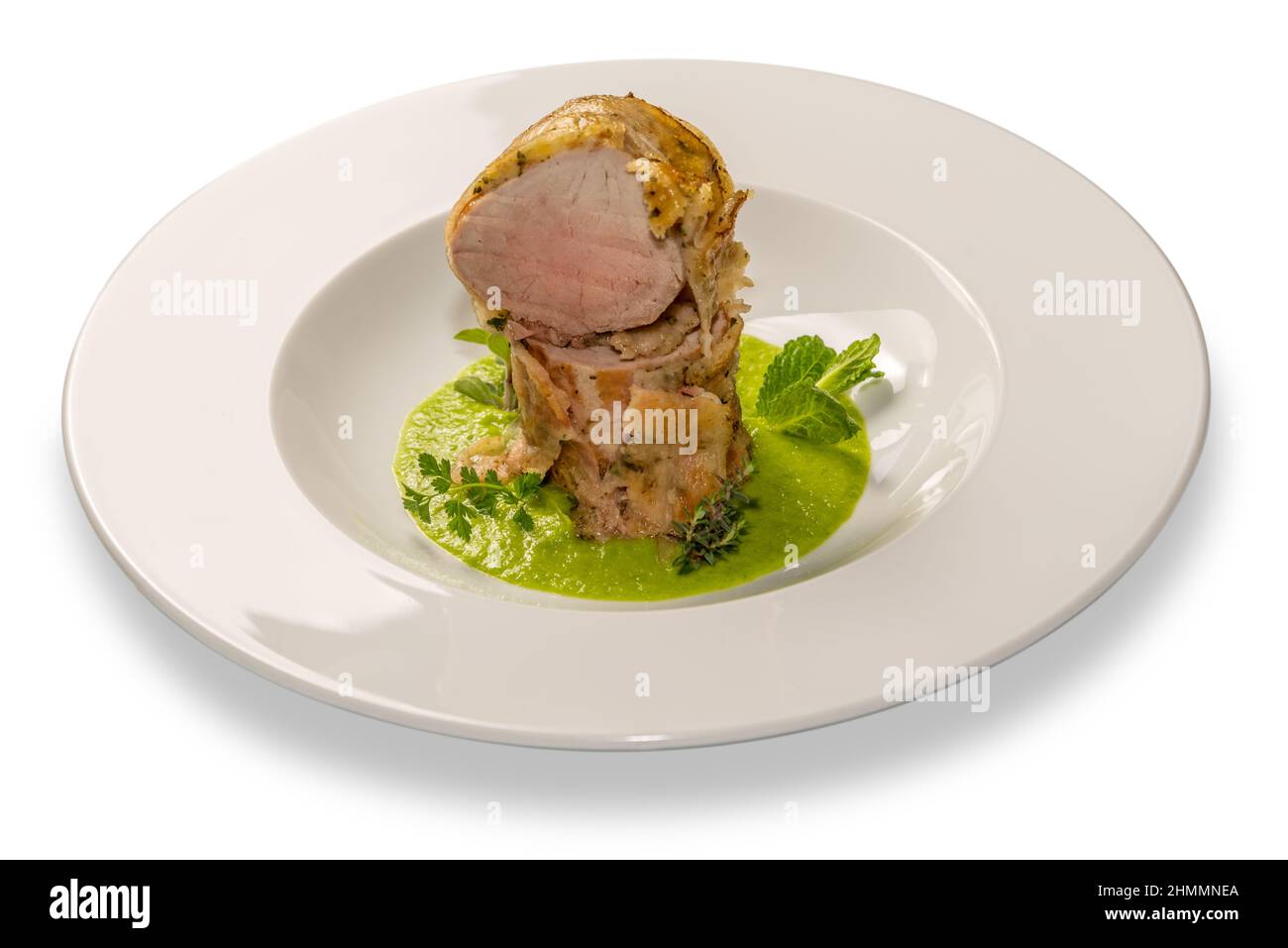 Baked pork fillet on pea cream and herbs in white plate isolated on