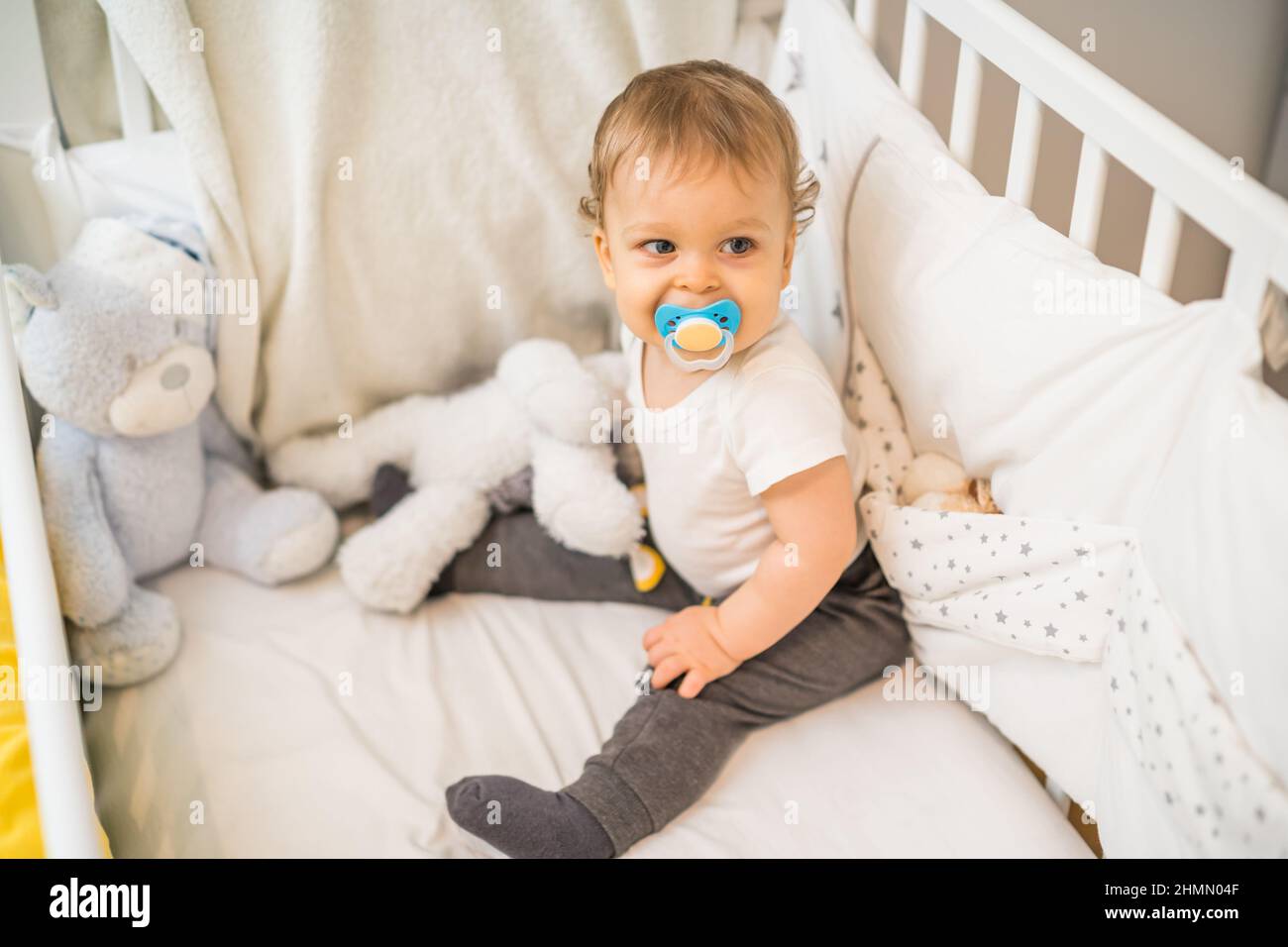 Image of cute baby boy with pacifier sitting in crib Stock Photo Alamy