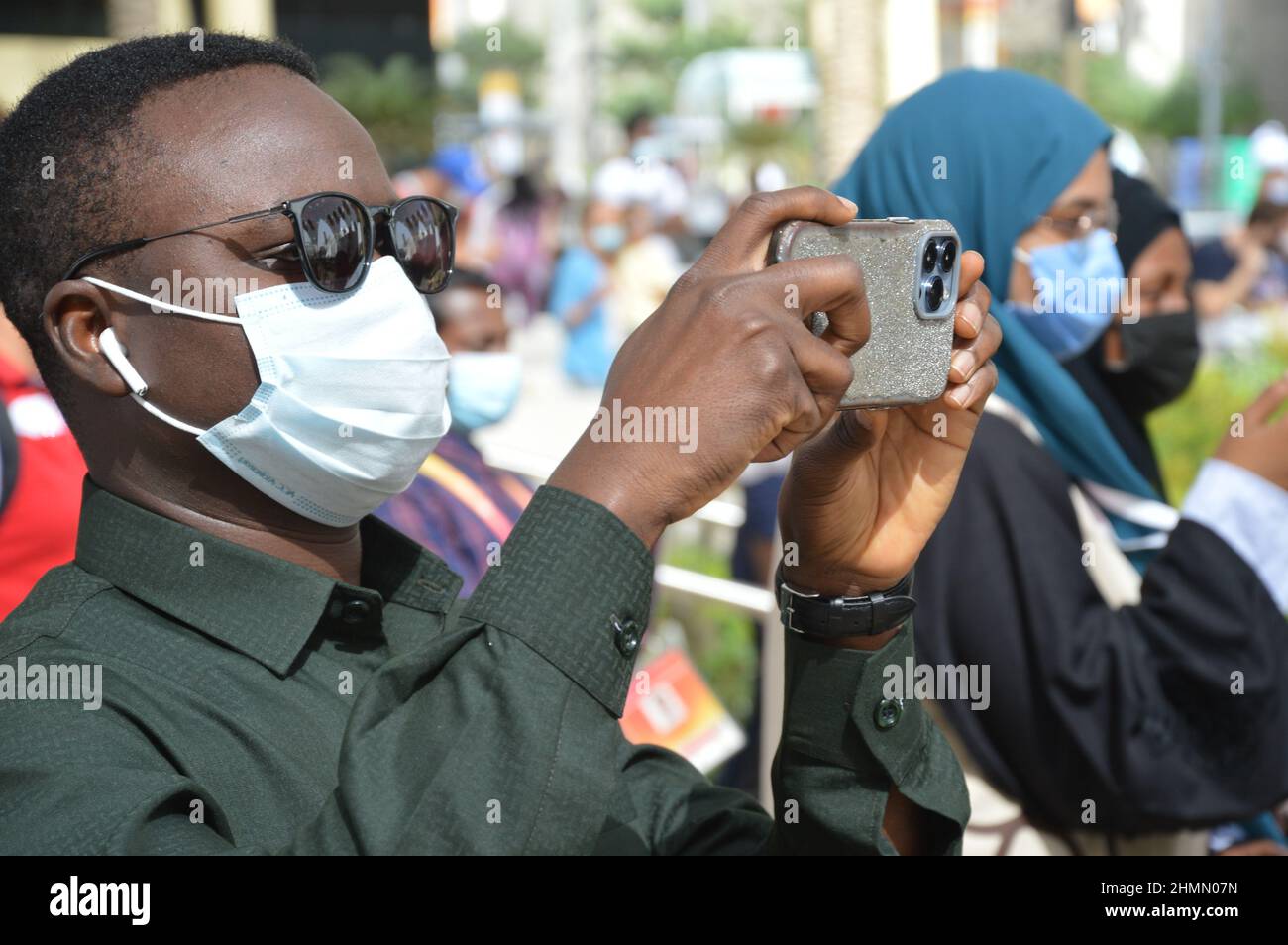 An Expo visitor from Africa wearing face mask and taking photos with his smartphone at Al Wasl Plaza at Expo 2020 Dubai in United Arab Emirates - February 1, 2022. Stock Photo