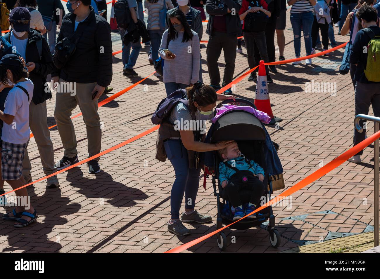 Hong Kong, China. 11th Feb, 2022. A domestic helper tries to keep a toddler cool as they have to queue for hours in the sun to undergo a mandatory testing at a temporary testing centre in Edinburgh Place in Central Hong Kong. Credit: Marc R. Fernandes /Alamy Live News Stock Photo