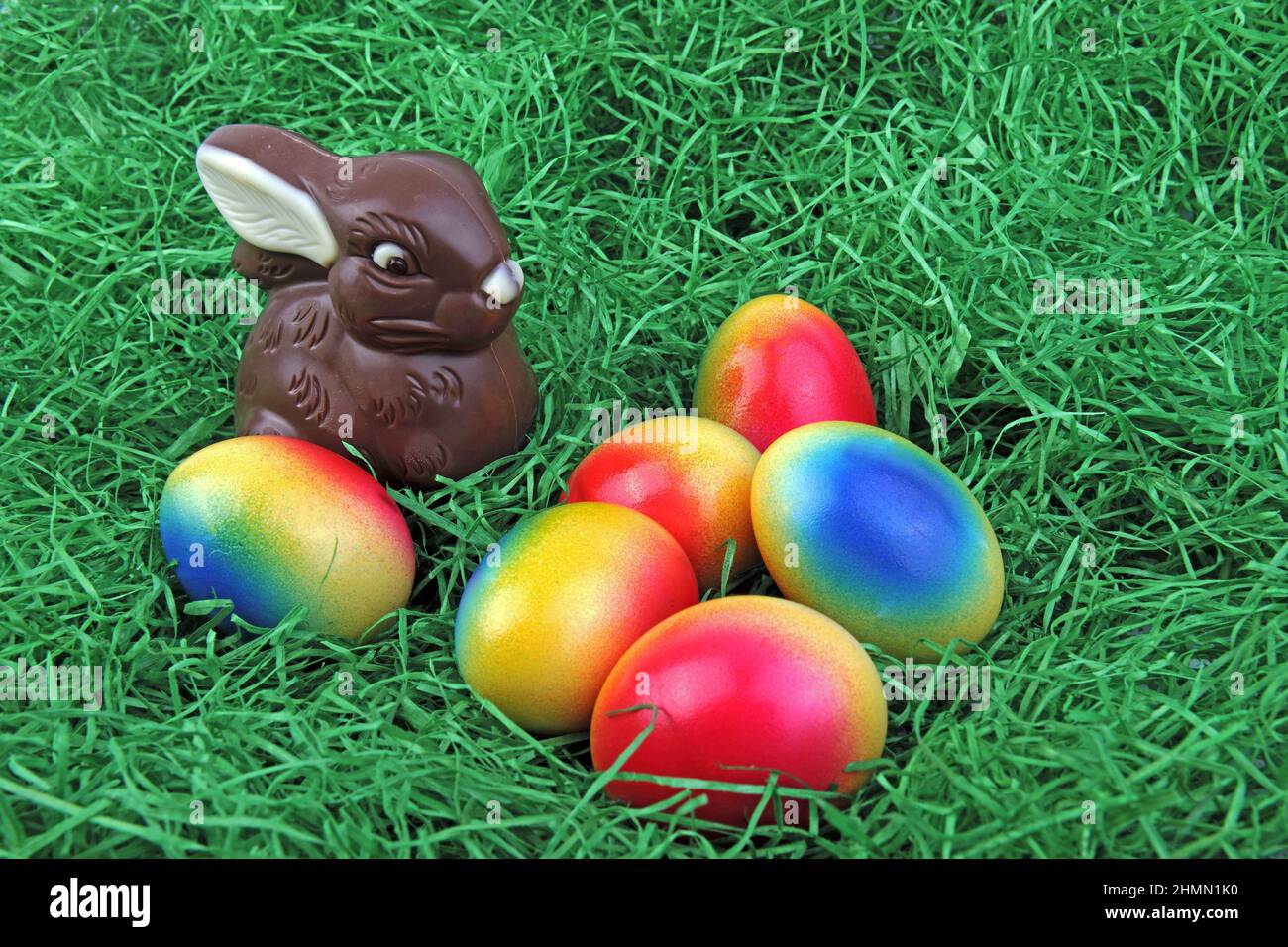 chocolate Easter bunny with brightly colored Easter eggs on grass Stock Photo