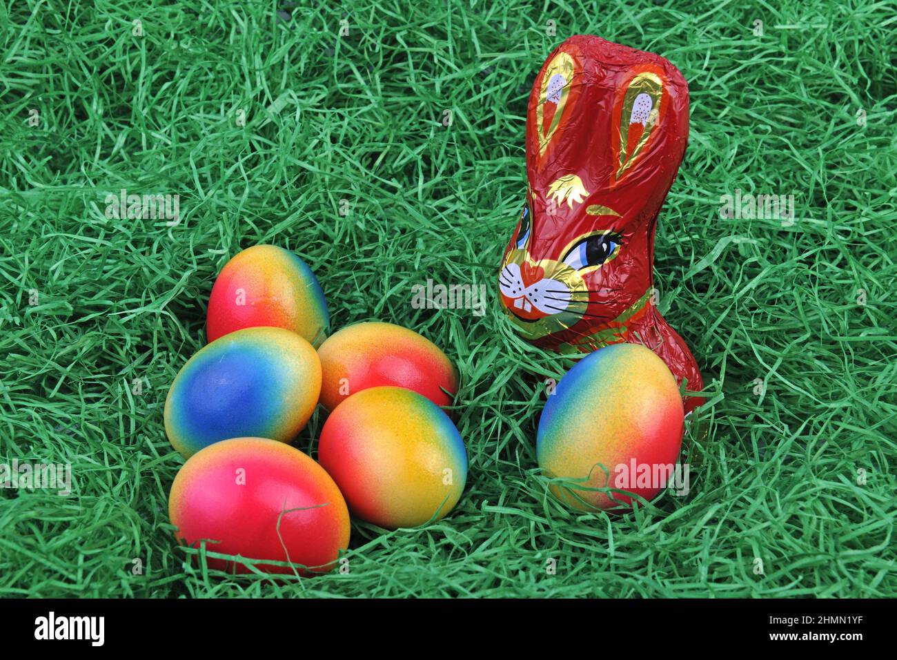 chocolate Easter bunny with brightly colored Easter eggs on grass Stock Photo