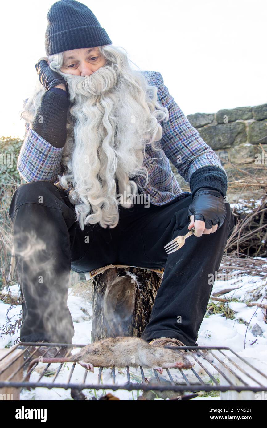 The homeless man grills a rat in the snowy outskirts of the city. Stock Photo