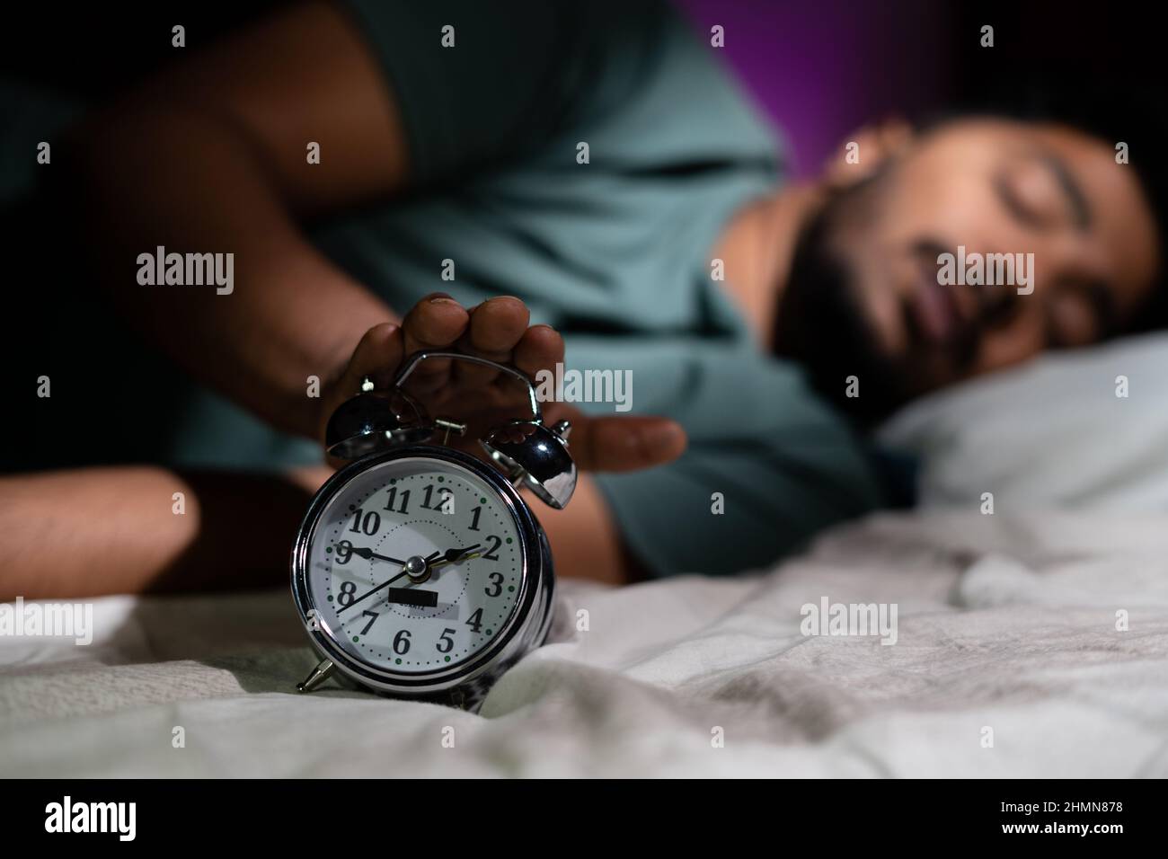 Focus on alarm, young man waking up early morning by turning off alarm - concept of active healthy lifestyle and morning routine. Stock Photo