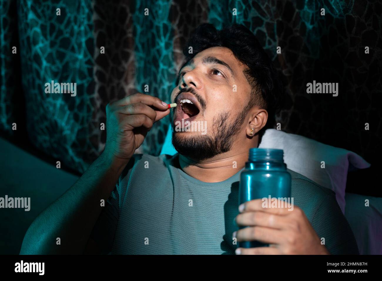Young man taking medicine pills or tablets on bed while sleeping at night - conept of insomnia, unhealthy lifestyle, depression and illness. Stock Photo