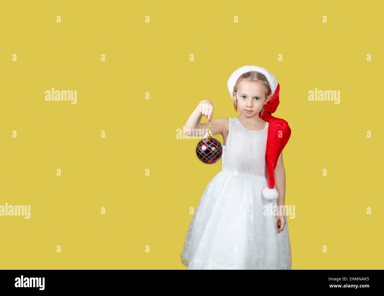 Adorable caucasian girl with a Christmas toy in hand smiling at the camera.A place for your text. Studio shot on a yellow background. The concept of N Stock Photo