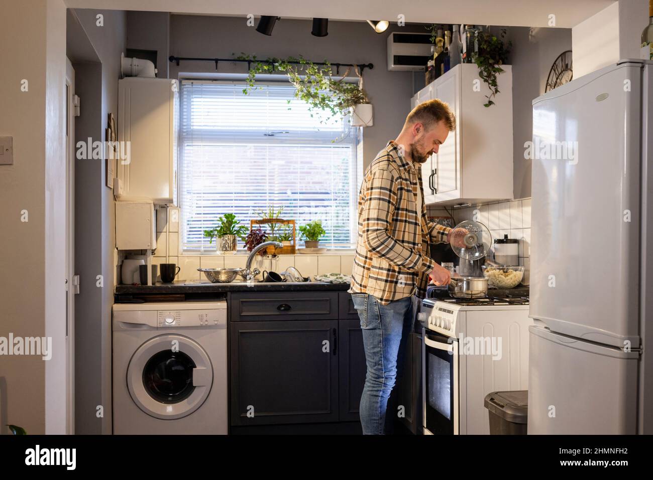 A side-view shot of a caucasian man standing in his kitchen, he is making pasta for lunch. Stock Photo