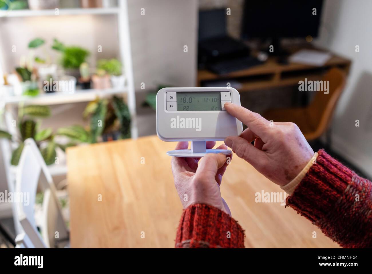 A point of view shot of an unrecognisable man holding a thermostat in his home. Stock Photo