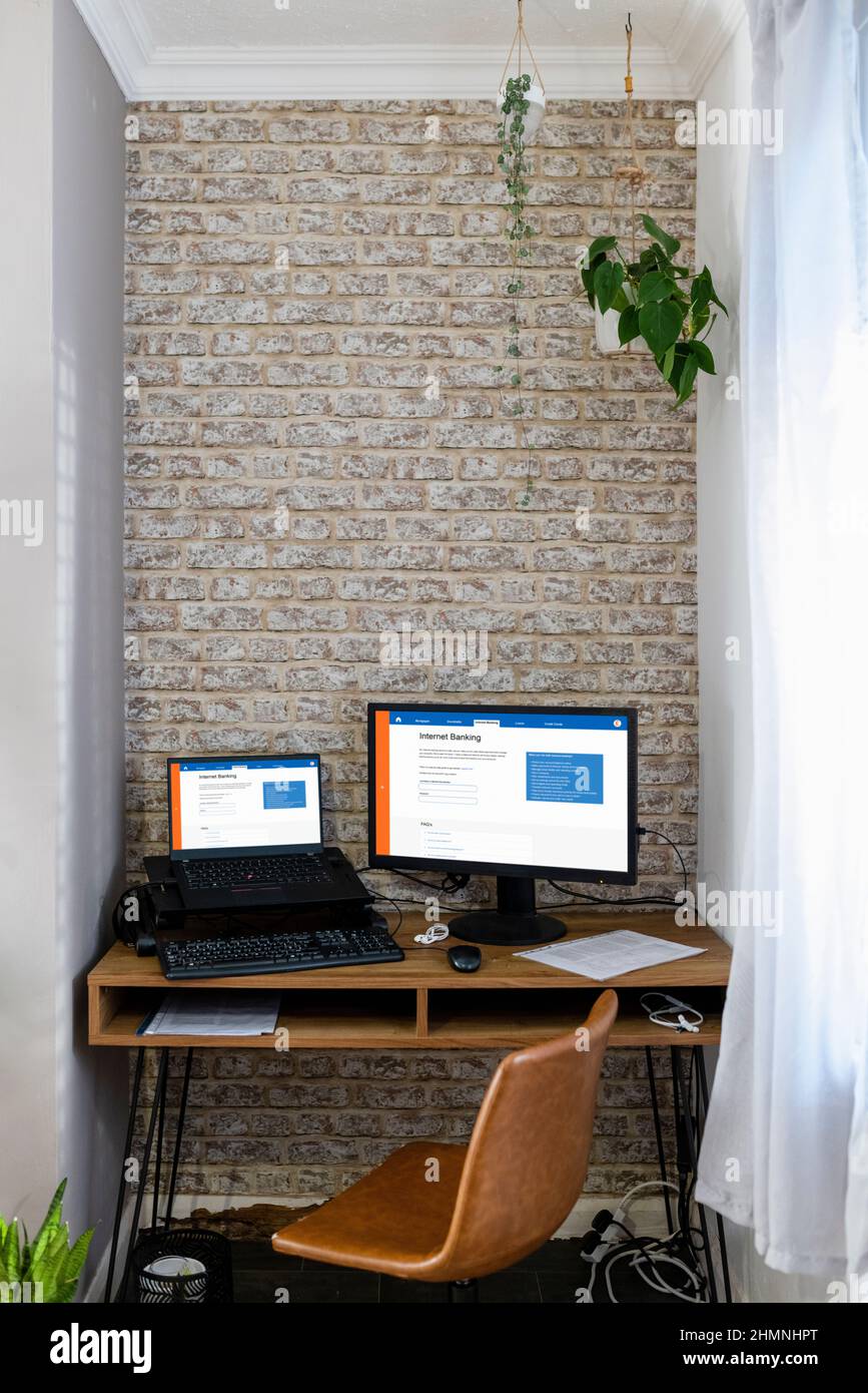 A shot of a home office workspace desk with two monitors, internet banking is displayed on the screens. Stock Photo