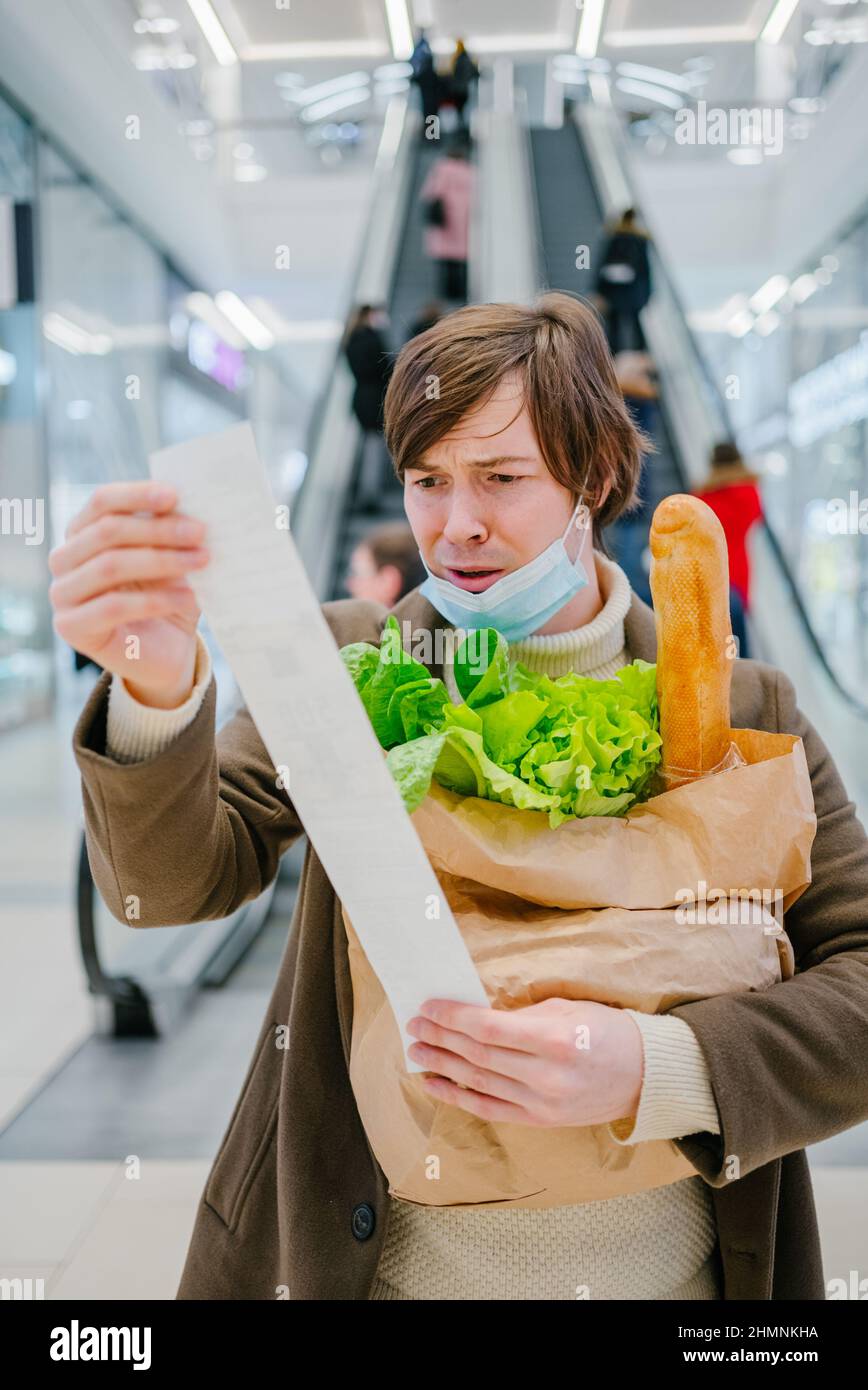 Man in a medical mask looks in horror at a check in a supermarket and holds