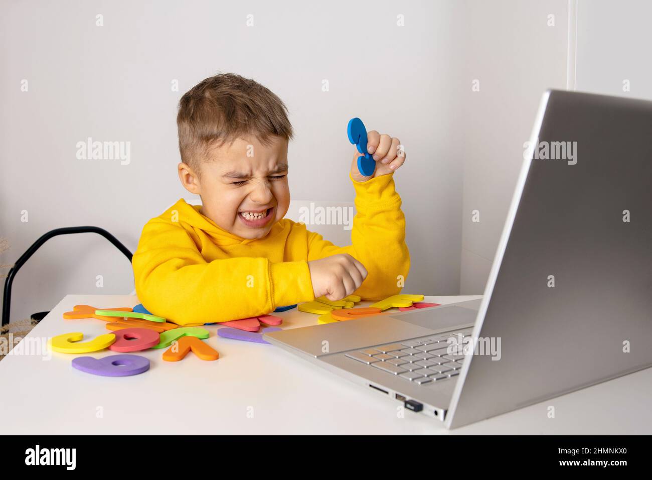 Little boy learning alphabet and numbers online, with laptop at home. Child is sad and stressed. Negative emotions, anger, stress, mental problems Stock Photo