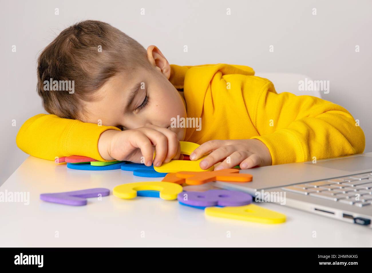 Little boy learning alphabet and numbers online, with laptop at home. Child is sad and tired. Negative emotions, stress, mental problems Stock Photo