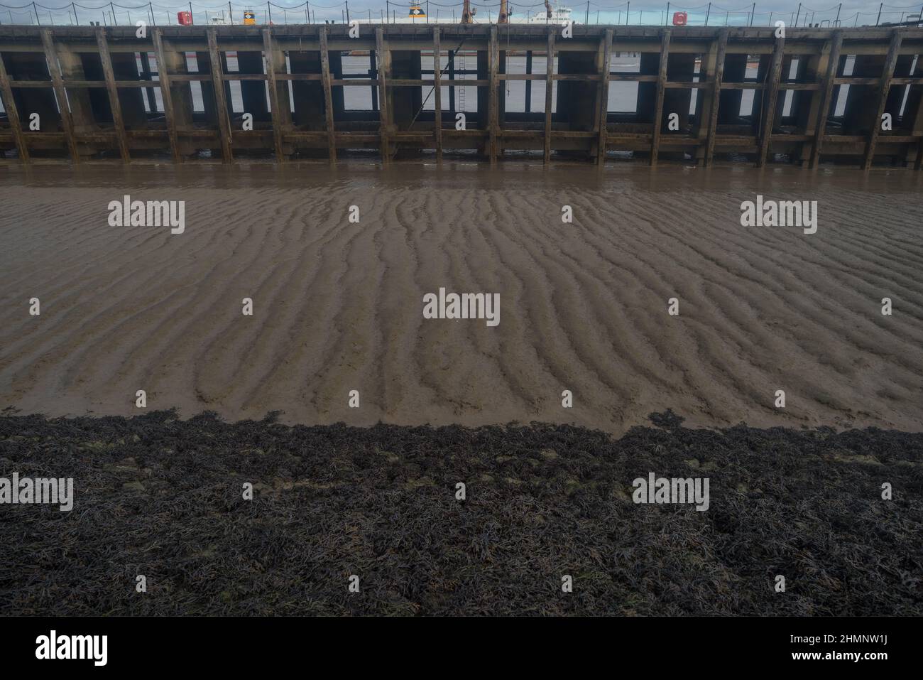 Region of unstable silt demarks area between pier and foreshore where seaweed cannot grow due to silt and currents Stock Photo