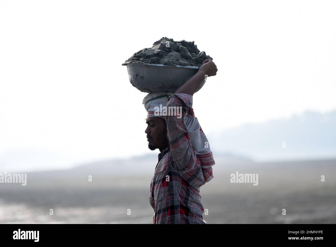 Guwahati, India. 07 February 2022. Laborer carries soil from a river bank as they filling