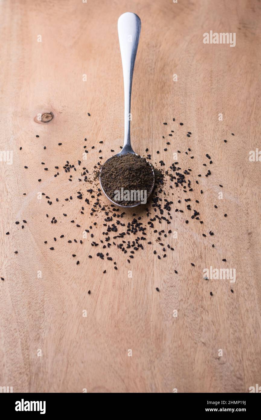 powdered and roasted black seeds, also known as black cumin or caraway or kalonji, in a spoon, with scattered seeds on a table top, shallow depth of f Stock Photo
