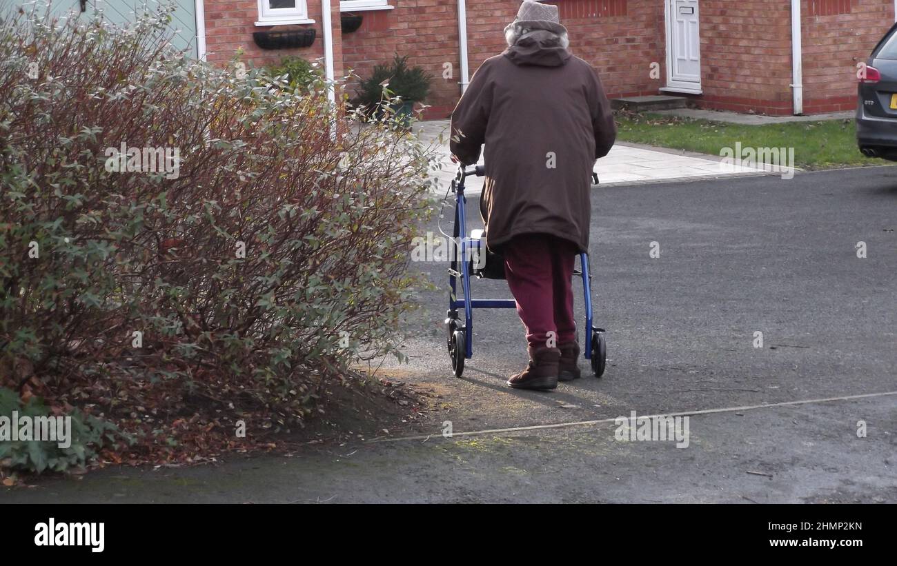 Rear view of mature women using a walking aid. Old lady using a mobility walker to aid walking. Stock Photo