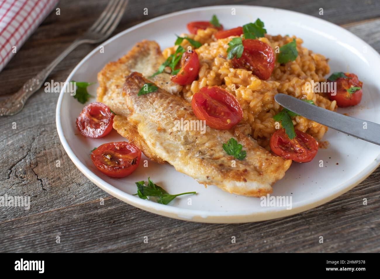 Roasted fish with tomato risotto on a plate on wooden table background Stock Photo
