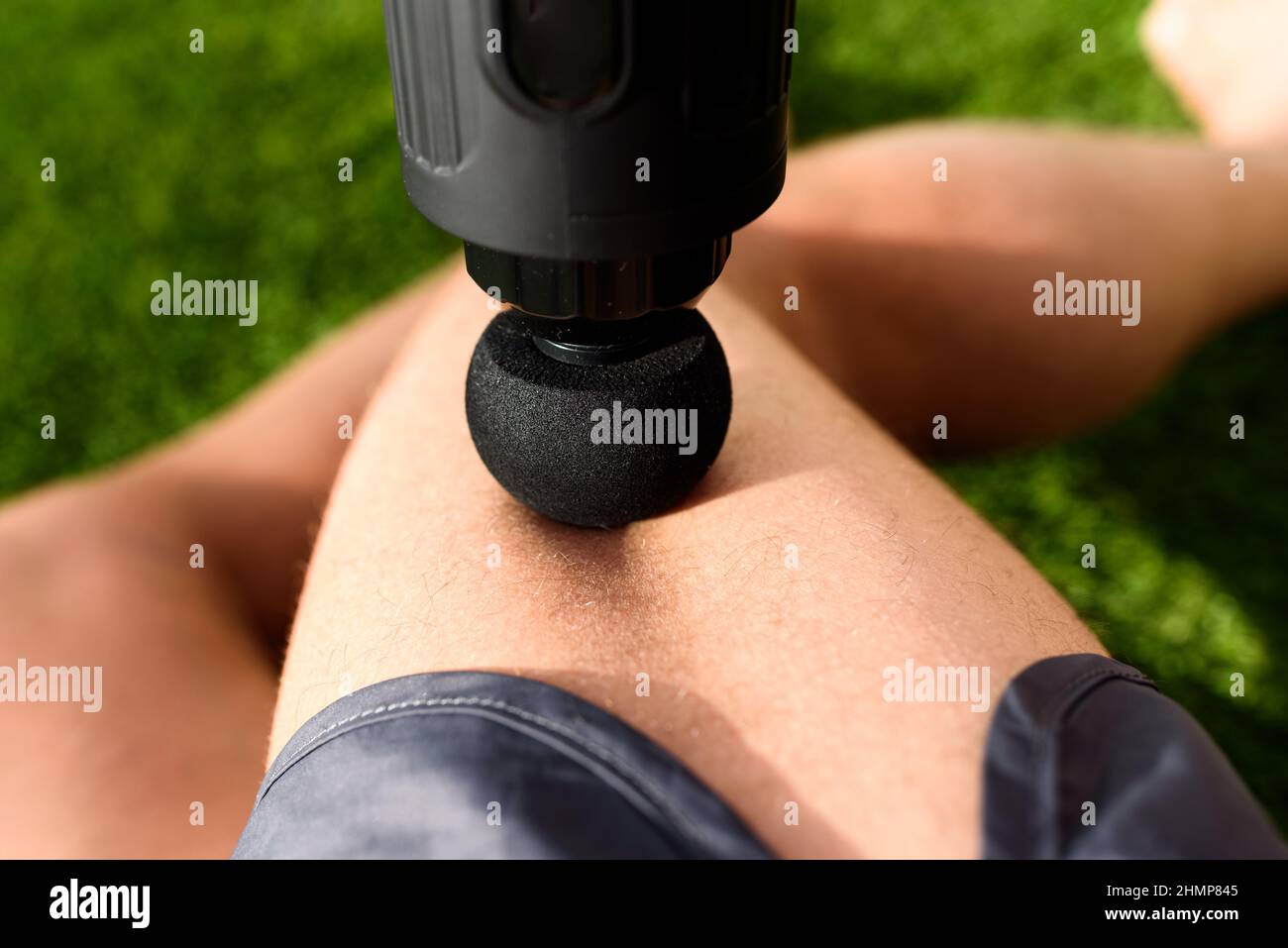 Athlete receives a massage with a percussion gun to relieve pain from muscle soreness in his legs. Stock Photo