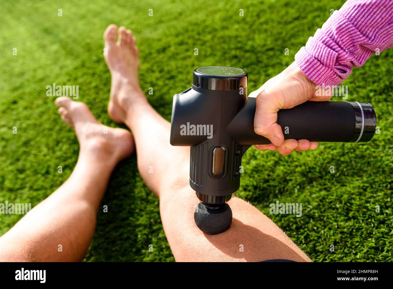 Athlete receives a massage with a percussion gun to relieve pain from muscle soreness in his legs. Stock Photo