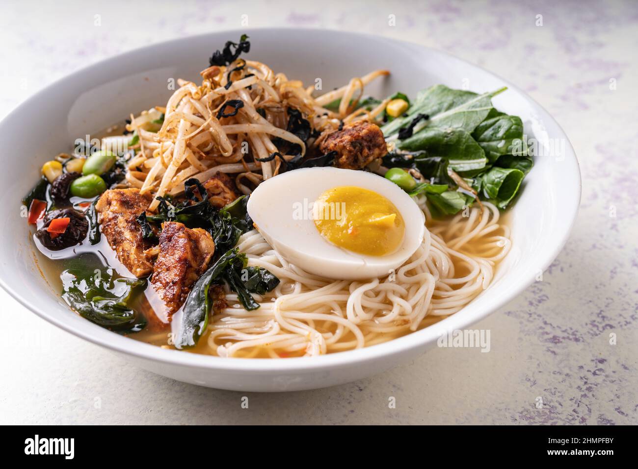 Asian fusion vegan meat-free ramen noodles with mushrooms, fermented tofu, sprout, beans, vegan egg and green pak choi leaves Stock Photo