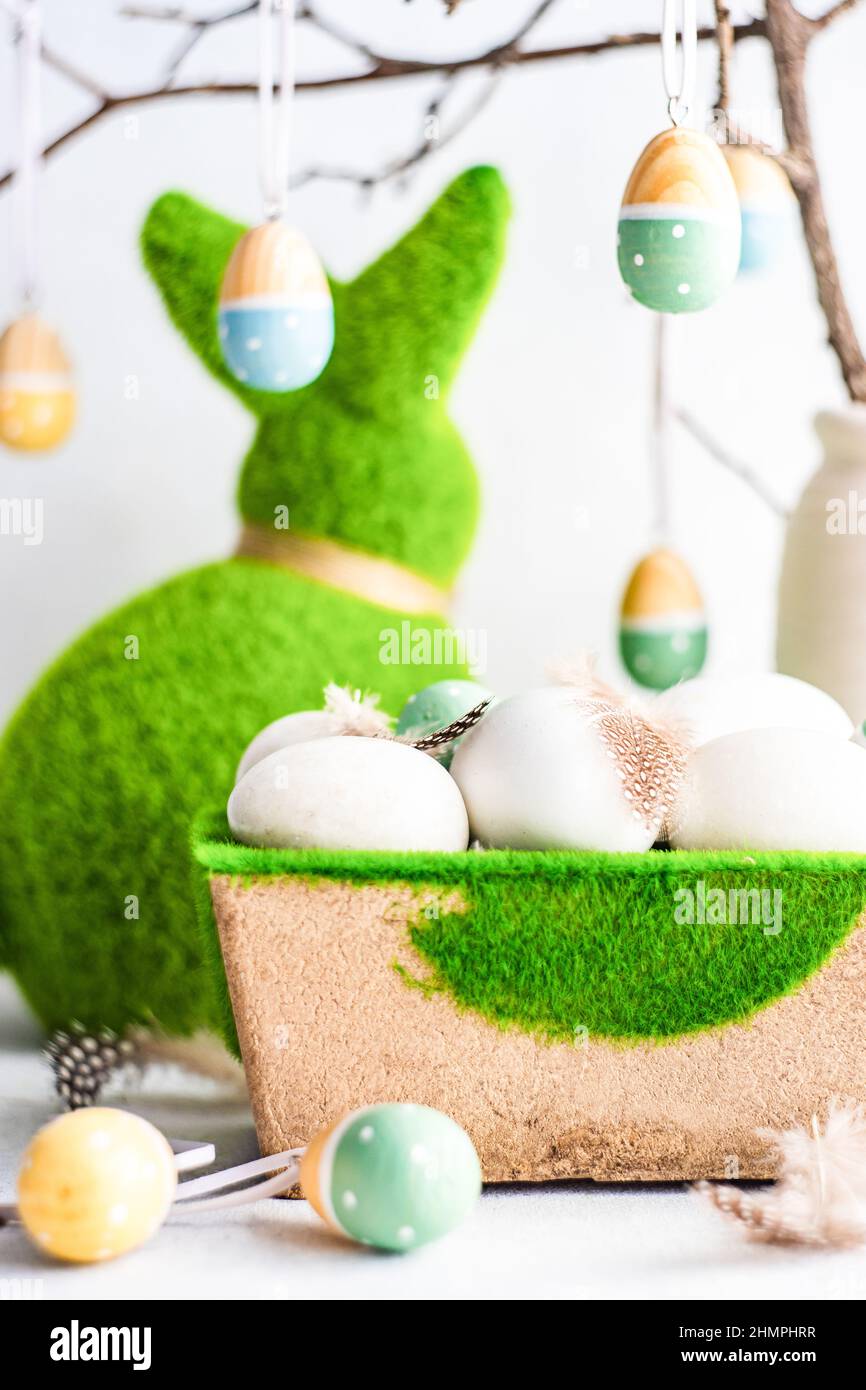 Easter egg decorations hanging on a branch next to an Easter bunny and a carton of eggs Stock Photo