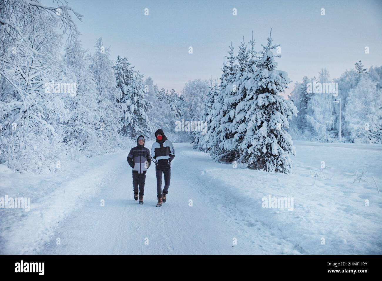 Two boys walking along a snow covered road in winter, Rovaniemi, Lapland, Finland Stock Photo