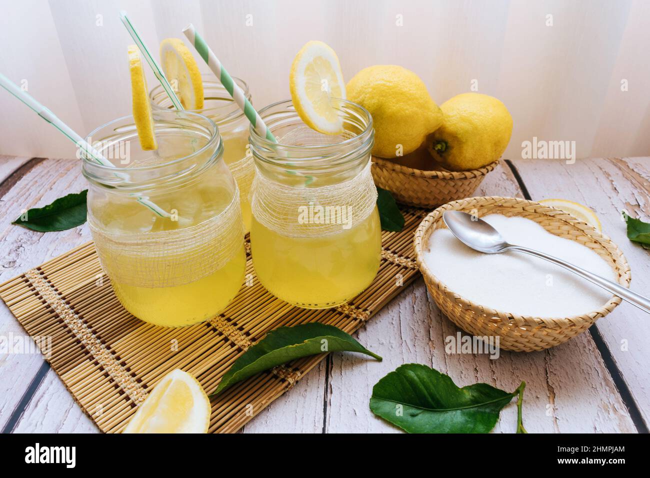 Three glasses of homemade lemonade on a table with fresh lemons and a bowl of sugar Stock Photo