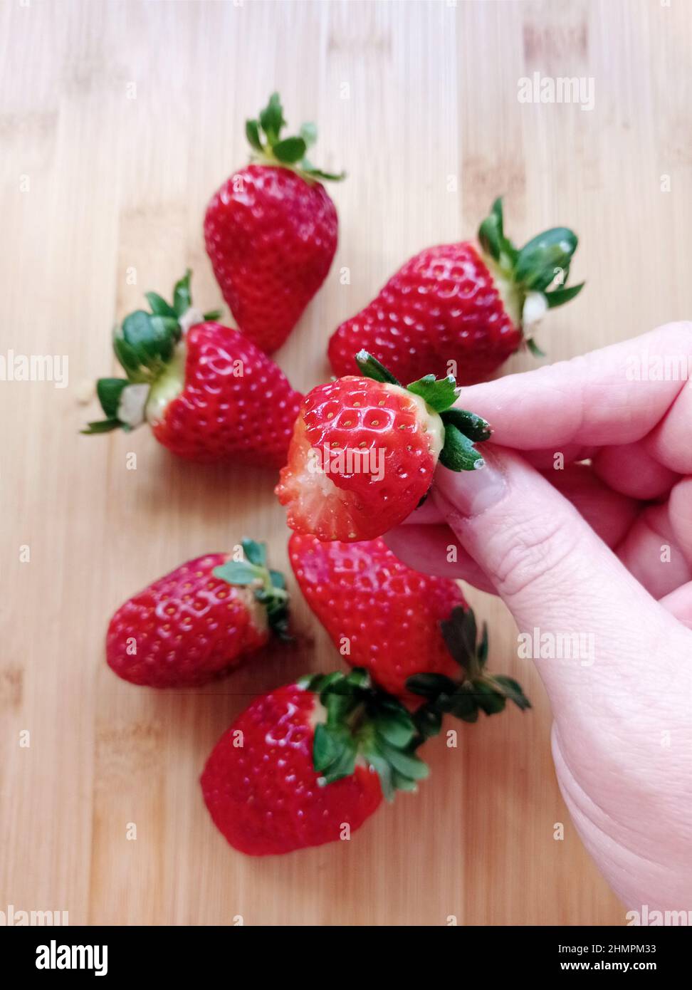 Hand holding fresh strawberry with a missing bite Stock Photo