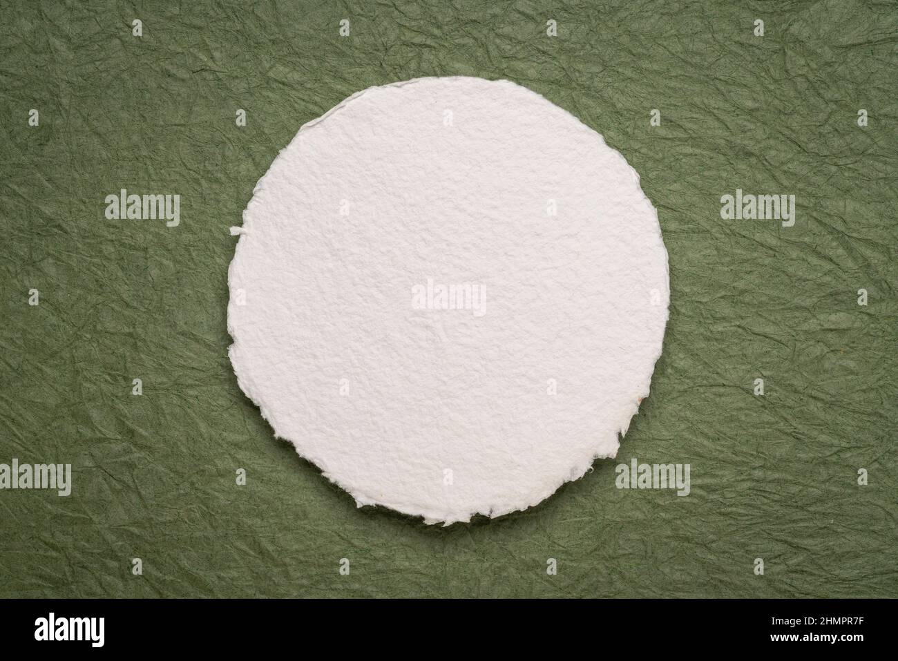 circular sheet of blank white watercolor paper against textured green paper Stock Photo