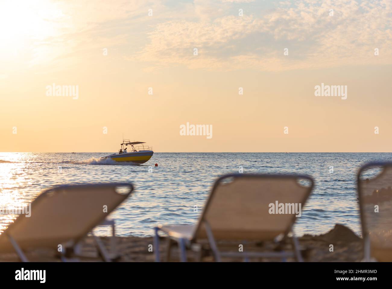 The backs of the sun loungers in front of the sea with a boat. Evening on the beach. Focus on the boat. Stock Photo