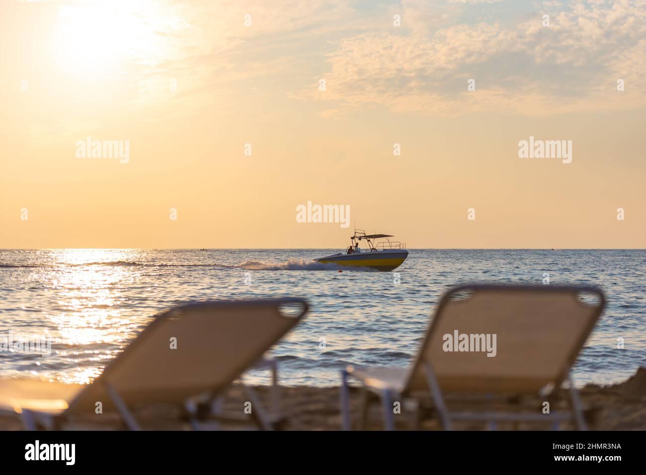The backs of the sun loungers in front of the sea with a boat. Evening on the beach. Focus on the boat. Stock Photo