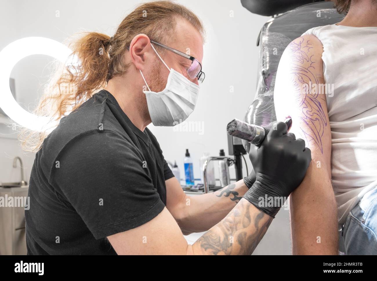 Premium Photo  A professional tattooer artist doing tattoo on the arm of a  young man by machine with black ink