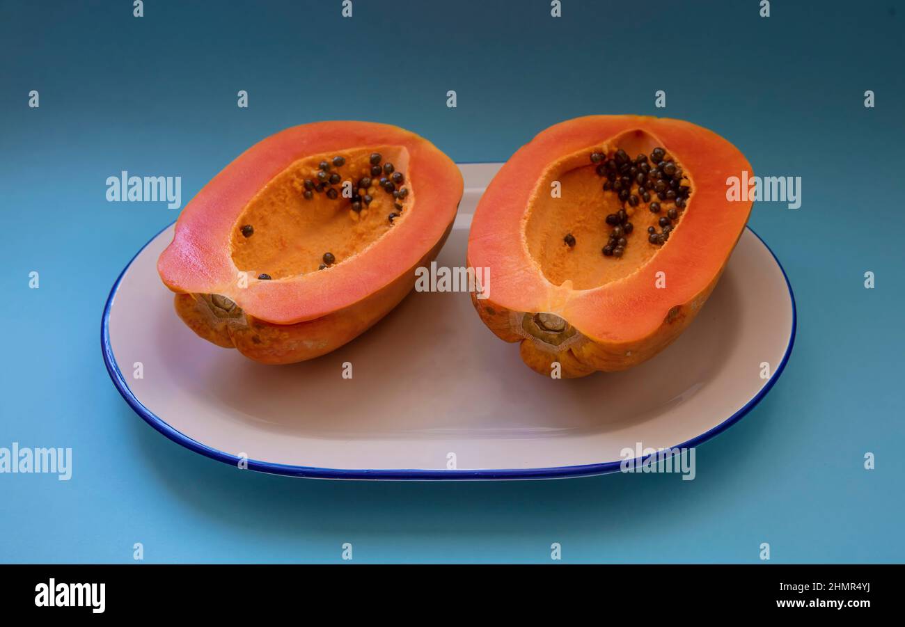 Papaya cut in half on white plate with blue border on blue background Stock Photo