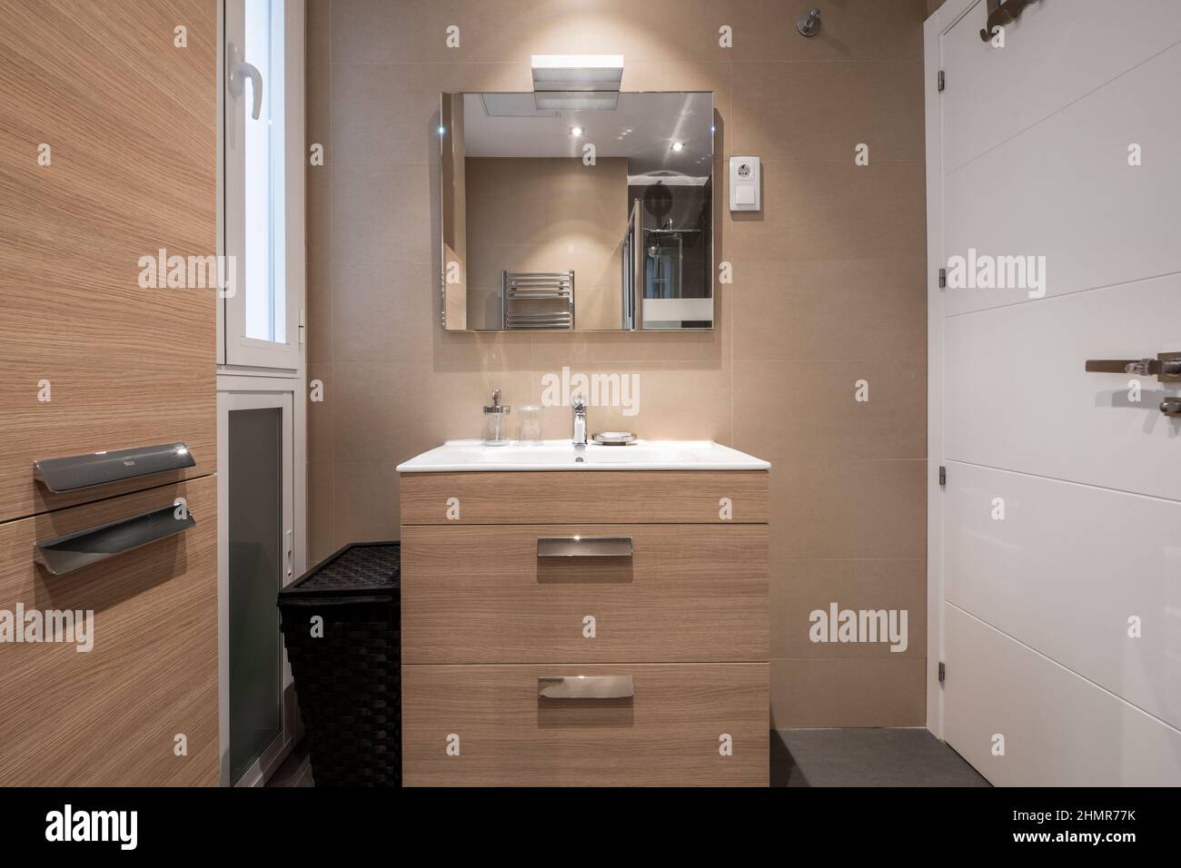 Bathroom with light woodgrain furniture, white porcelain sink, square frameless mirror and white door Stock Photo