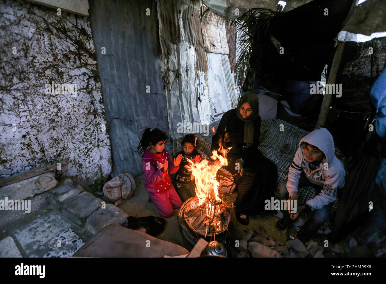 A Palestinian family sits around the fire to keep themselves warm ...