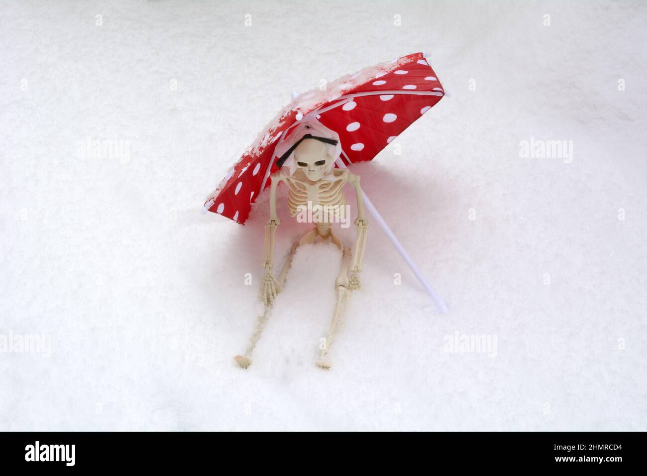 Sitting skeleton shielded by red parasol with white polka dots during snow storm Stock Photo