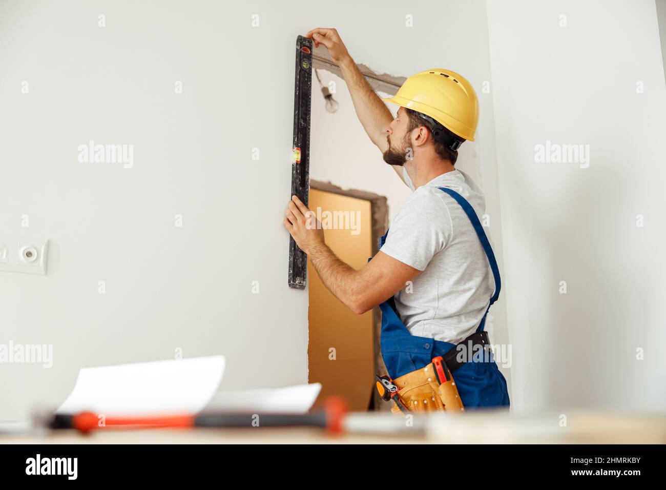 Hard working handyman, builder in uniform measuring the wall using bubble level Stock Photo