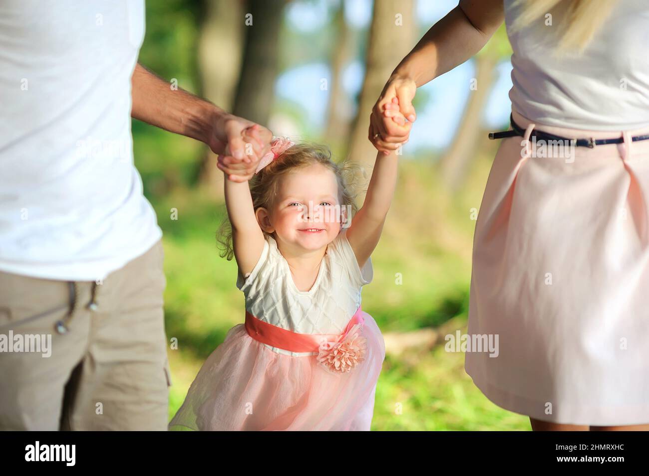 Happy family walks in a beautiful spring park, parents hold their daughter by the hands, healthy outdoor recreation Stock Photo
