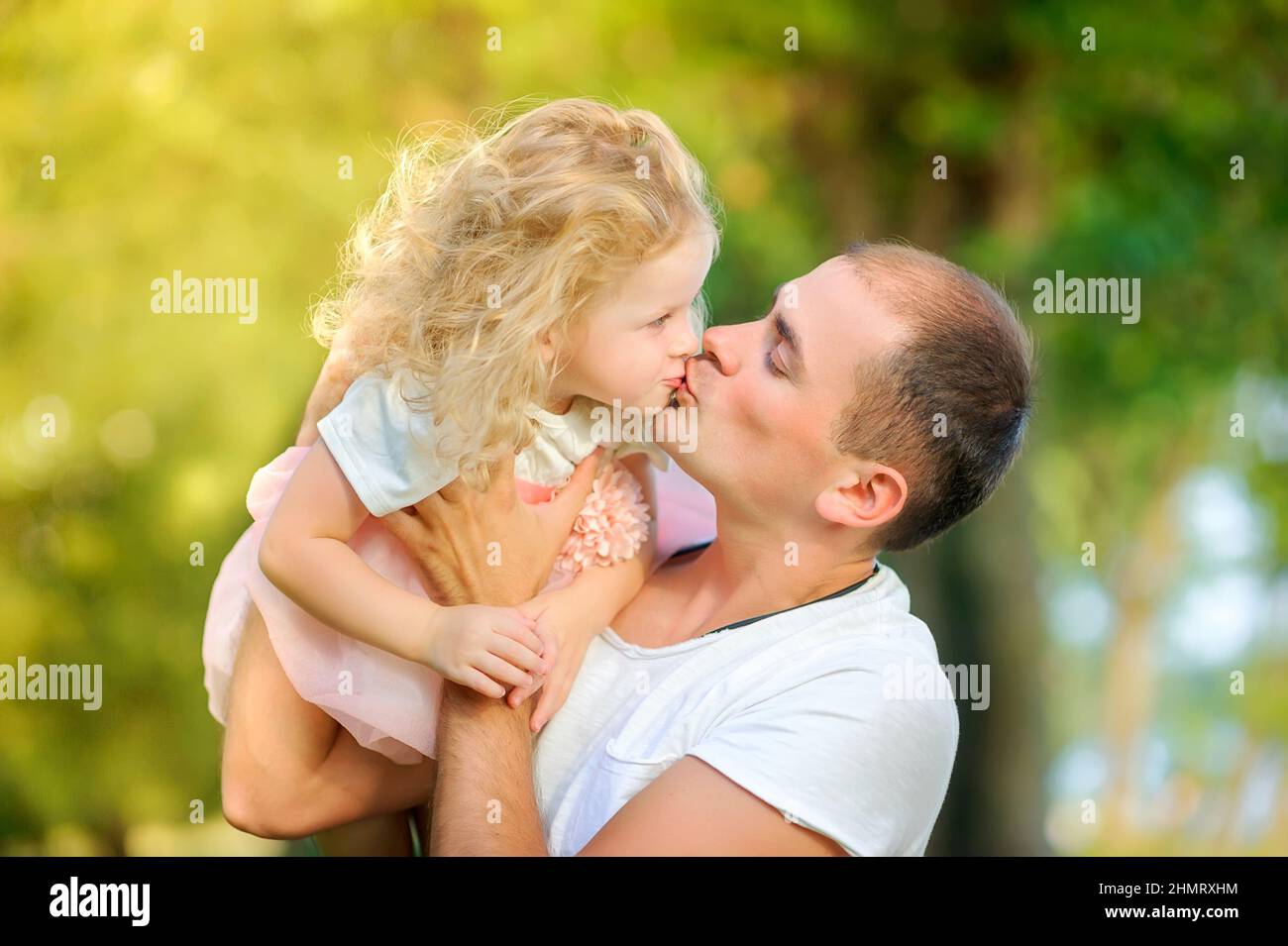 Happy family in a beautiful spring park, dad holds a daughter in his arms and kisses Stock Photo