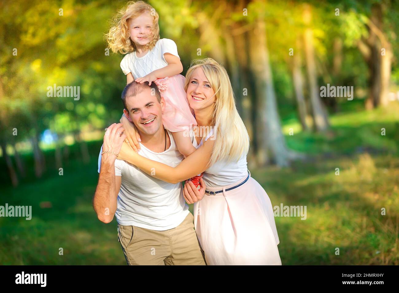 Happy family in a beautiful spring park, daughter around dad's neck, healthy outdoor recreation Stock Photo