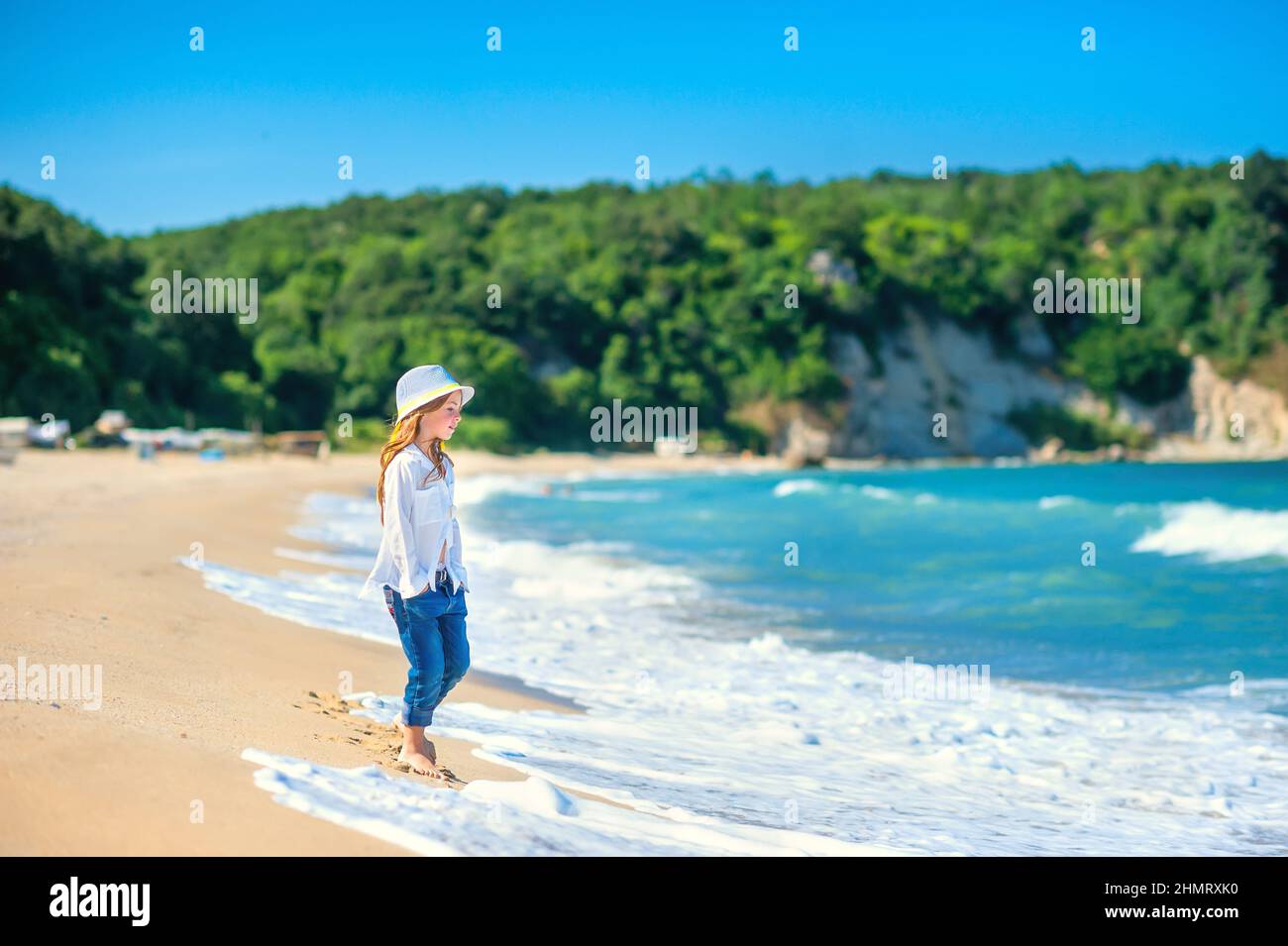 beautiful little girl in a beach hat walks along the seashore on a sunny day, healthy rest by the sea Stock Photo