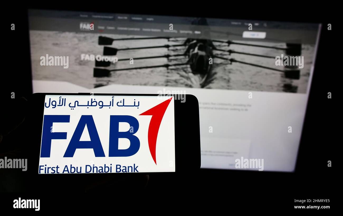 Person holding smartphone with logo of financial company First Abu Dhabi Bank (FAB) on screen in front of website. Focus on phone display. Stock Photo